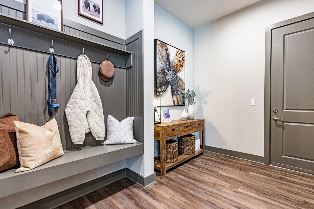 A modern entryway with a gray bench, coat hooks, and a wooden console table with a vase and a plant.