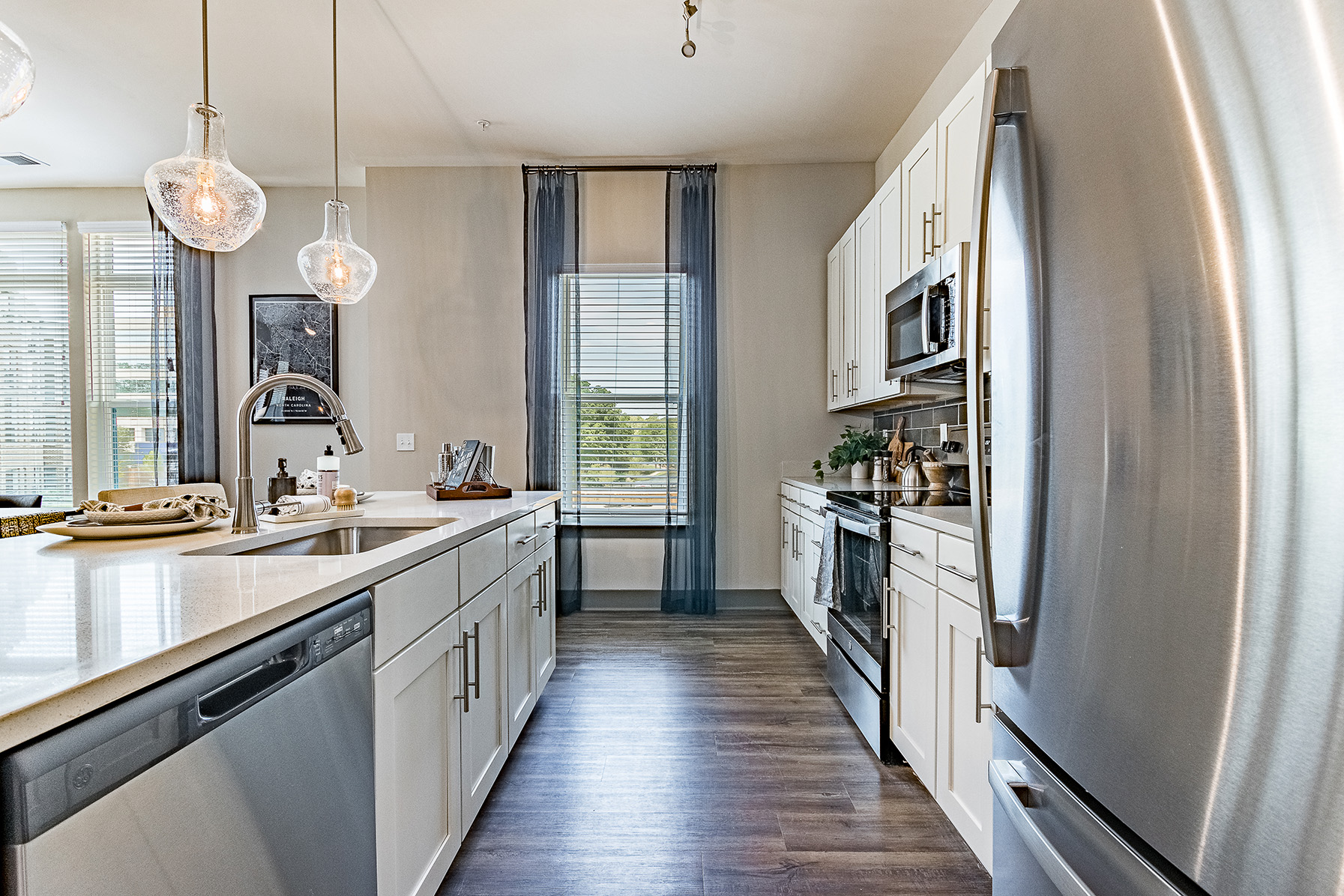 A modern kitchen with white cabinets, stainless steel appliances, and a large window with a view of trees and a blue sky.