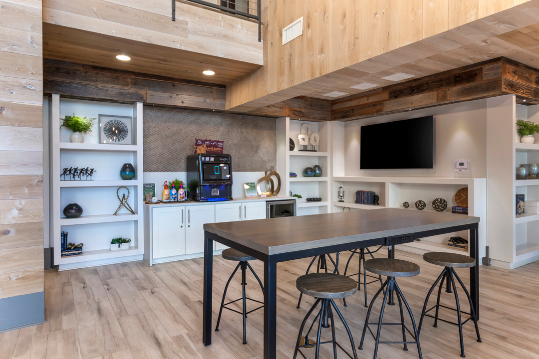 Recreation are with large TV, bar seating, white cabinets, and gray backsplash.